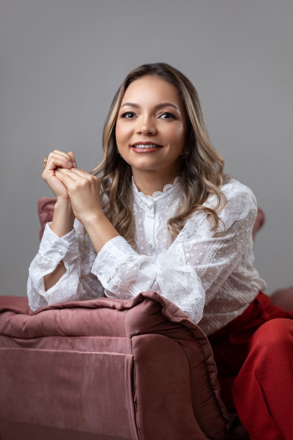Sileny Reis sentada em uma poltrona rosa, de blusa de renda branca
